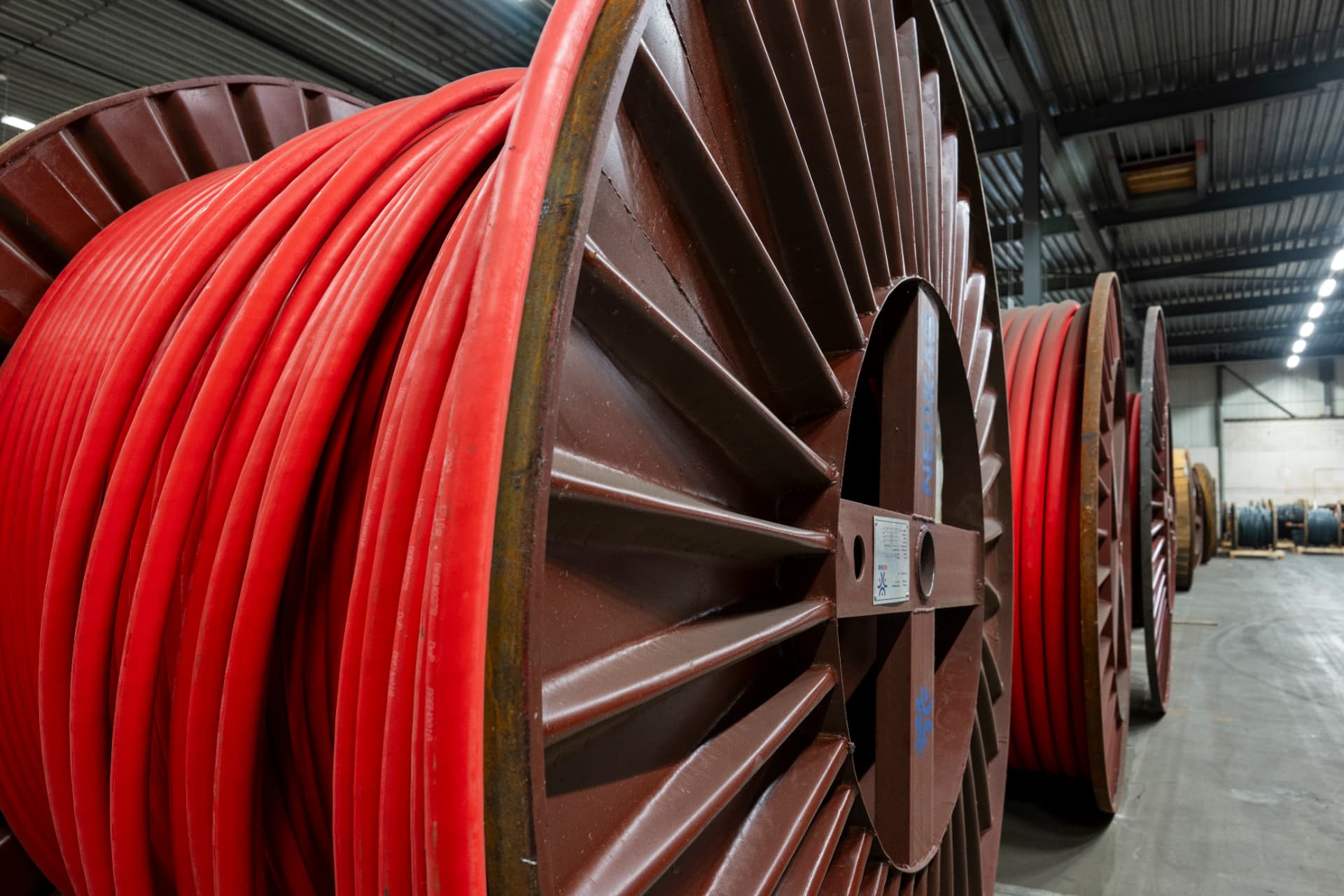 Large cable spools wound with red cable, stored in an ATIRIS warehouse